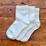 Three pairs of white ribbed crew socks arranged overlapping on a rustic wooden surface.