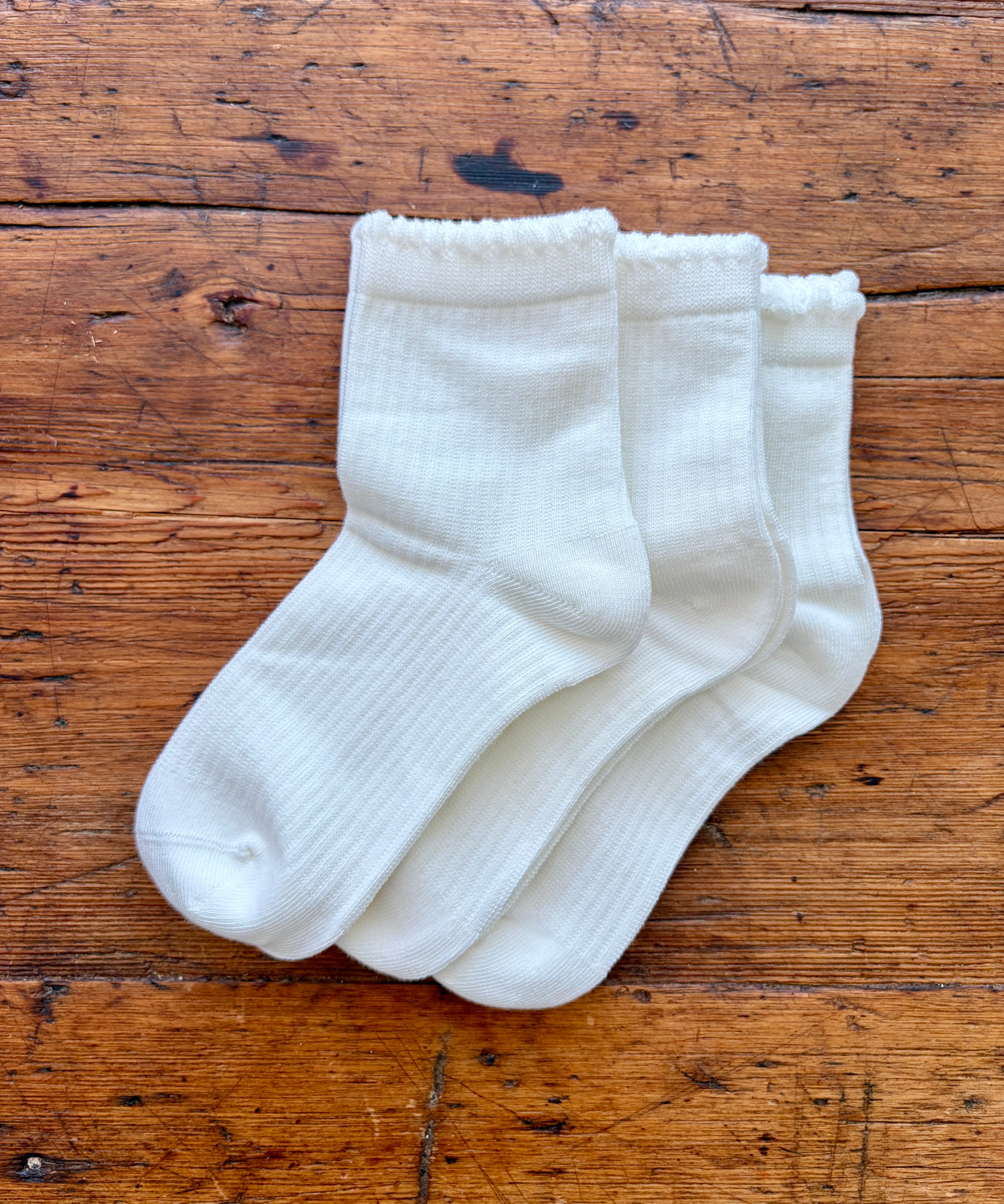 Three pairs of white ribbed crew socks arranged overlapping on a rustic wooden surface.
