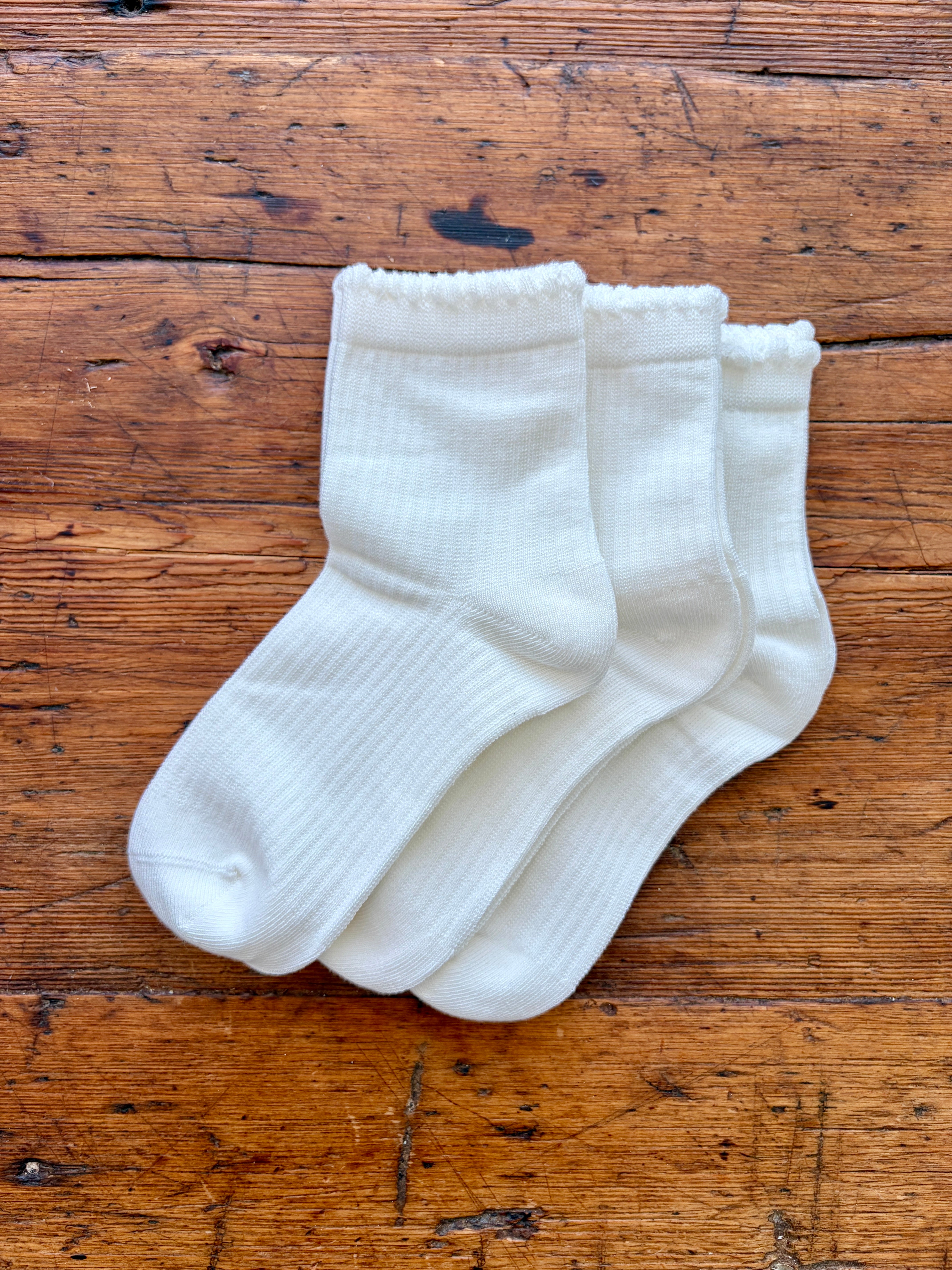 Three pairs of white ribbed crew socks arranged overlapping on a rustic wooden surface.