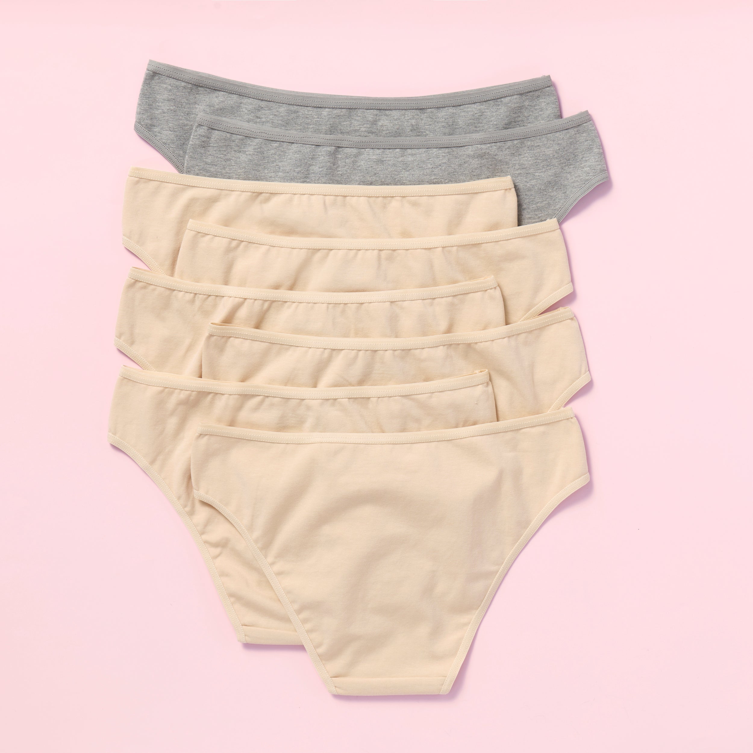 Eight pairs of women's underwear in beige and gray on a pink background