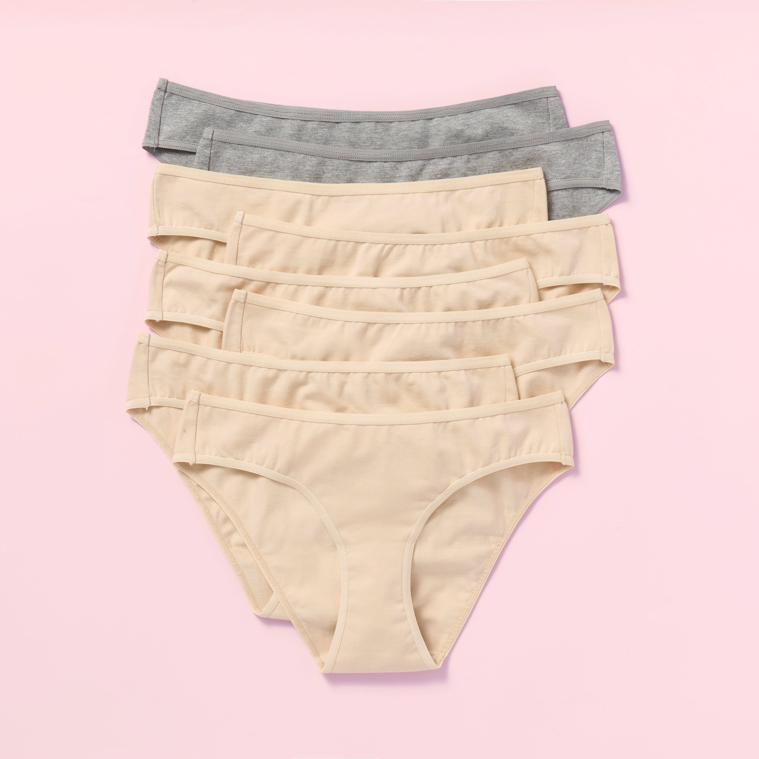 Eight pairs of women's underwear in beige and gray on a pink background