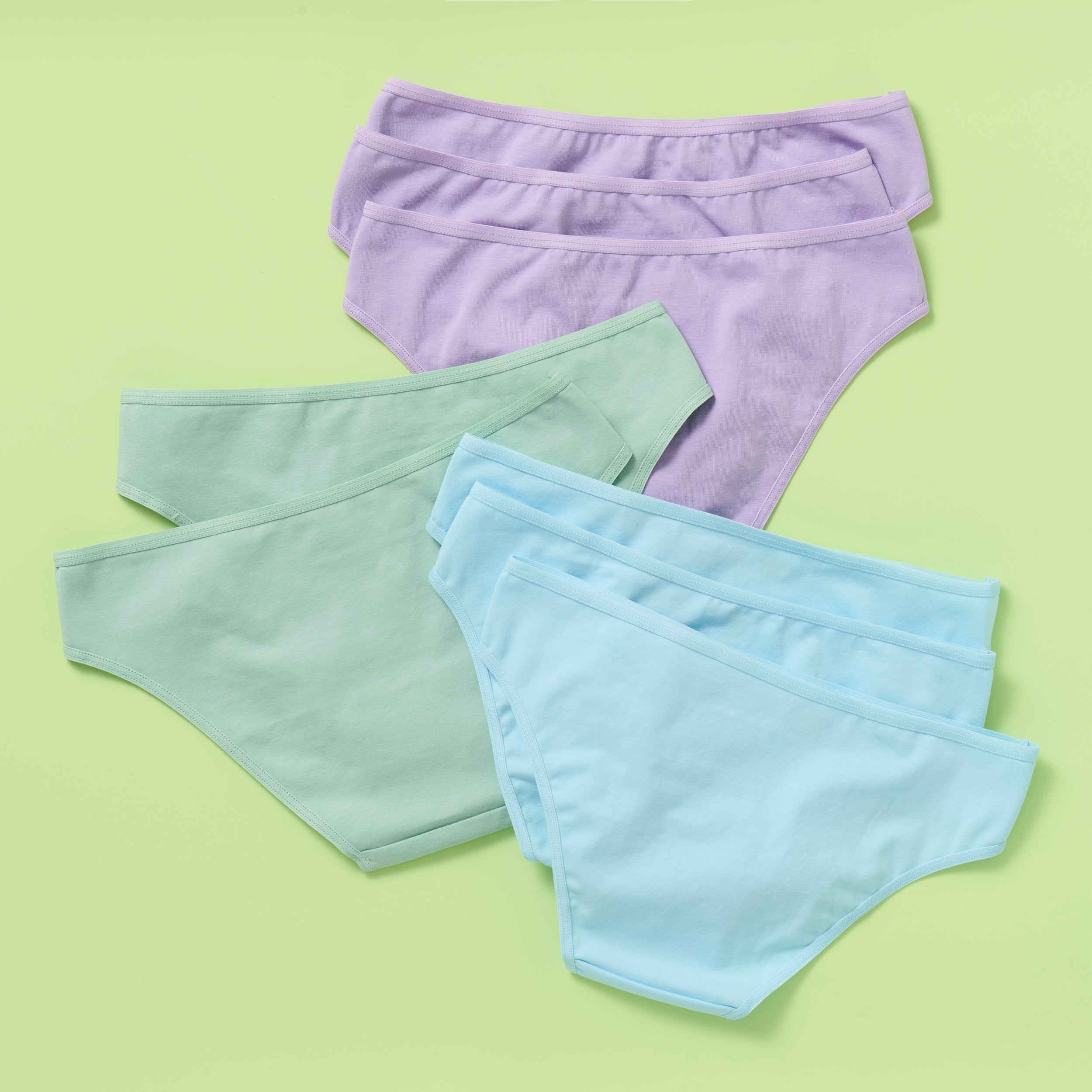 The back of eight pairs of women's underwear in purple, green, and blue on a light green background 