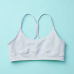 Tink Sports Bra by Yellowberry in a soft brushed nylon blend in a super mild grey, Storm. A Classicly designed bra with full support that ensures all-day ease and comfort. Our Storm colorway is a great neutral. Lay down image of Front Tink Storm against a turquoise background.