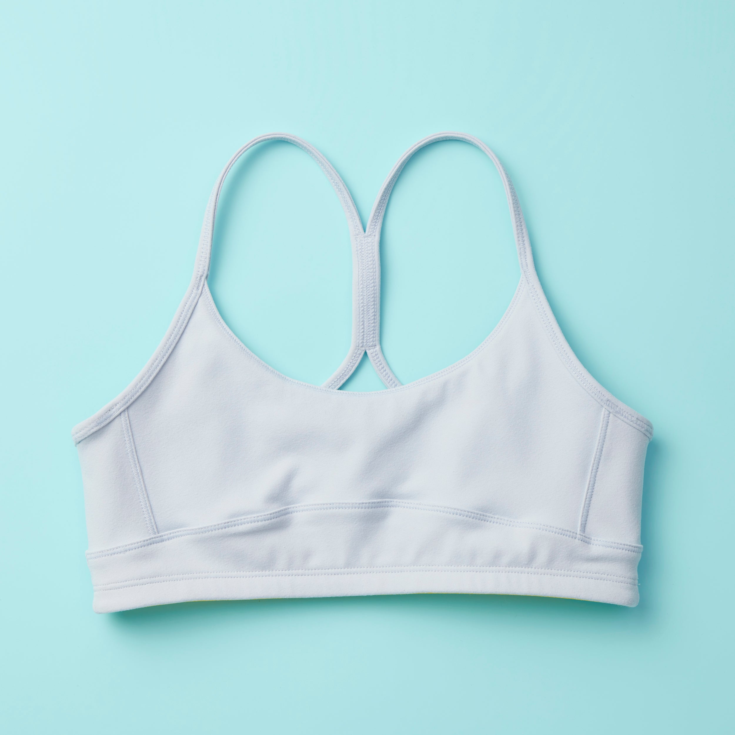 Tink Sports Bra by Yellowberry in a soft brushed nylon blend in a super mild grey, Storm. A Classicly designed bra with full support that ensures all-day ease and comfort. Our Storm colorway is a great neutral. Lay down image of Front Tink Storm against a turquoise background.