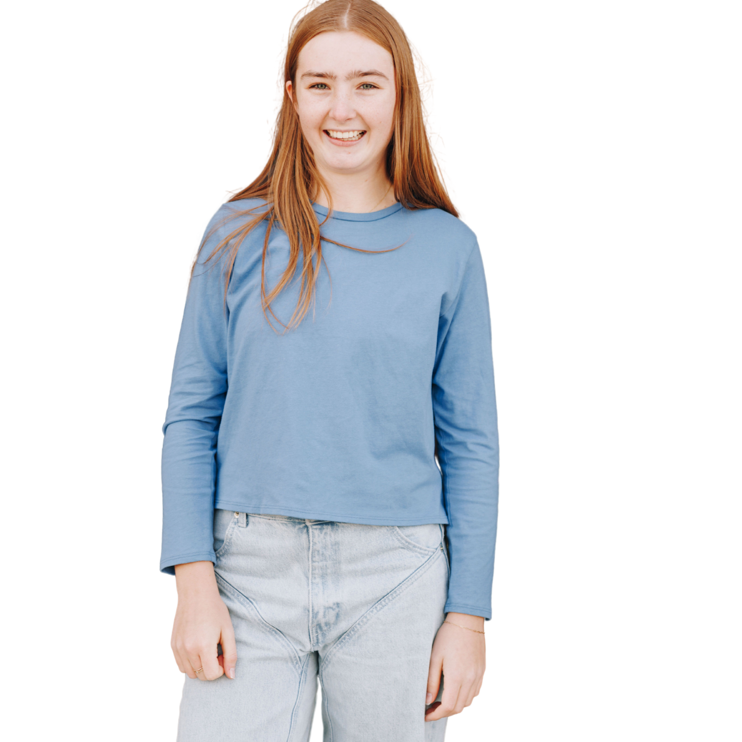 Girl smiling and laughing at the camera wearing an ocean blue color long sleeve cotton t-shirt on top with light wash blue jeans on bottom