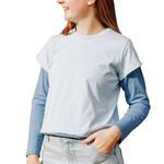Girl wearing a layered light blue cotton t-shirt on top of a long sleeved ocean blue cotton t-shirt. One hand is in her jeans pocket, and she is smiling away from the camera
