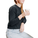 Photo of a girl sitting down holding her coffee and wearing a long sleeve lack whisper cotton t-shirt. 