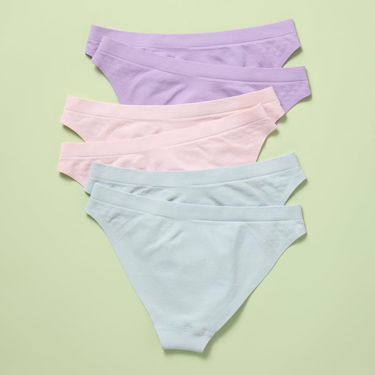 Six pairs of pastel-colored underwear on a light green background