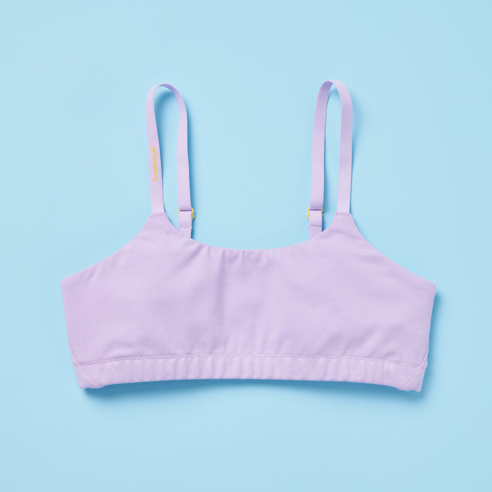 Pipit Huckleberry Cotton Training Bra for gils by Yellowberry with logo written on the strap and is a lavender bra with yellow hardware blue background front image