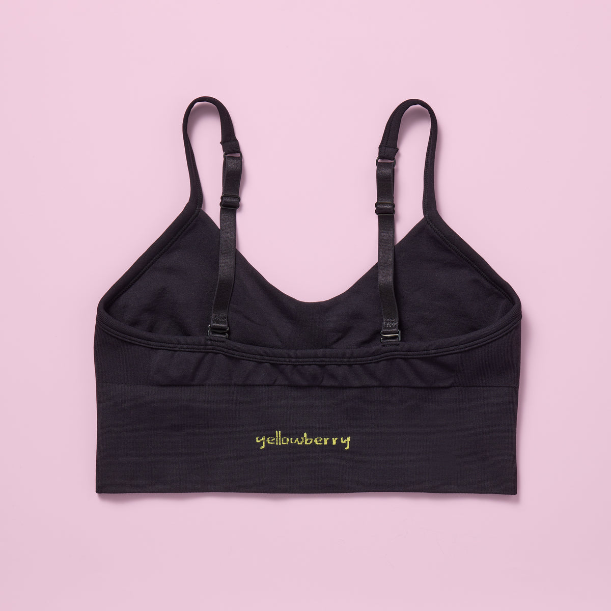 Black bra with adjustable straps on a pink background, featuring the Yellowberry brand.