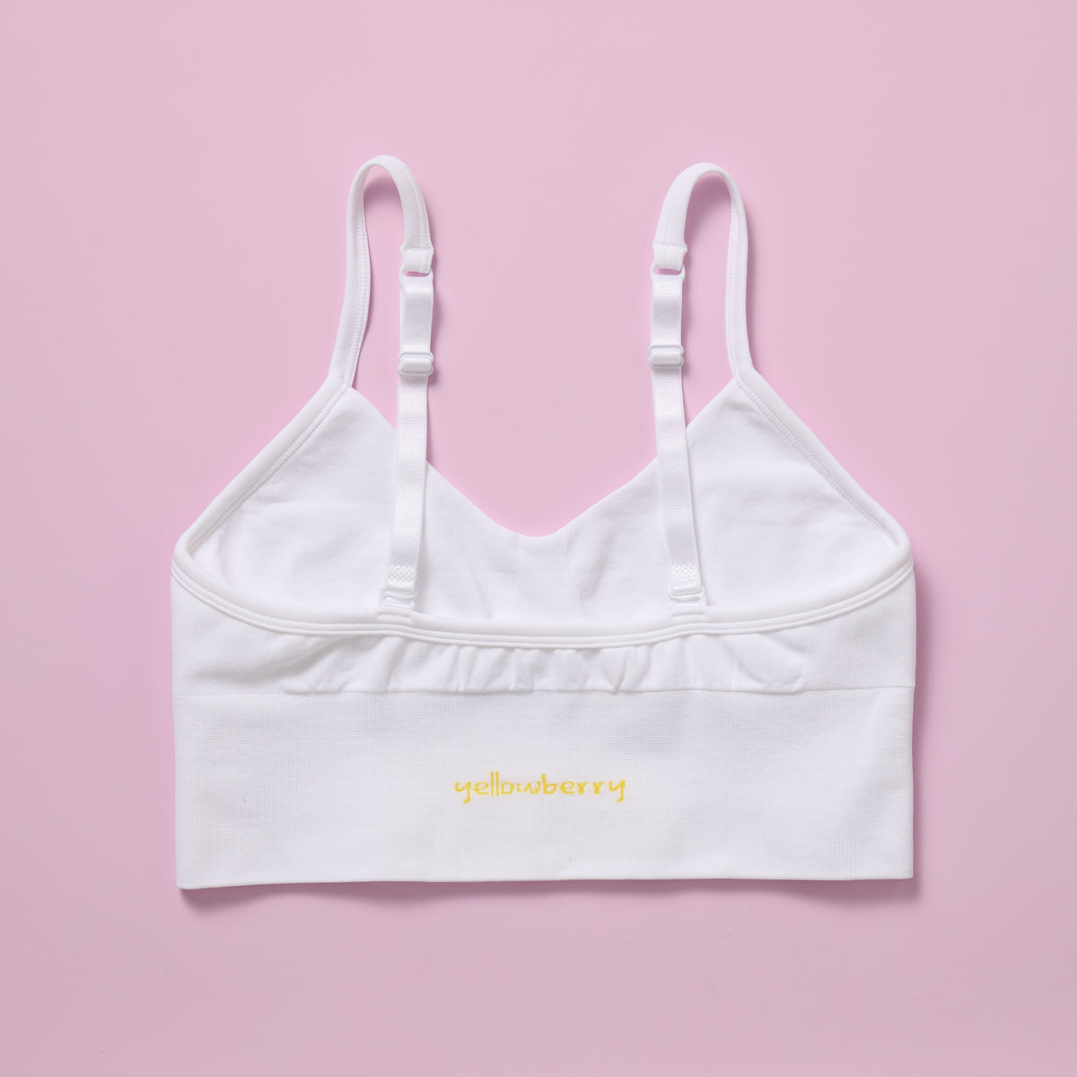 White sports bra with thin straps on a pink background