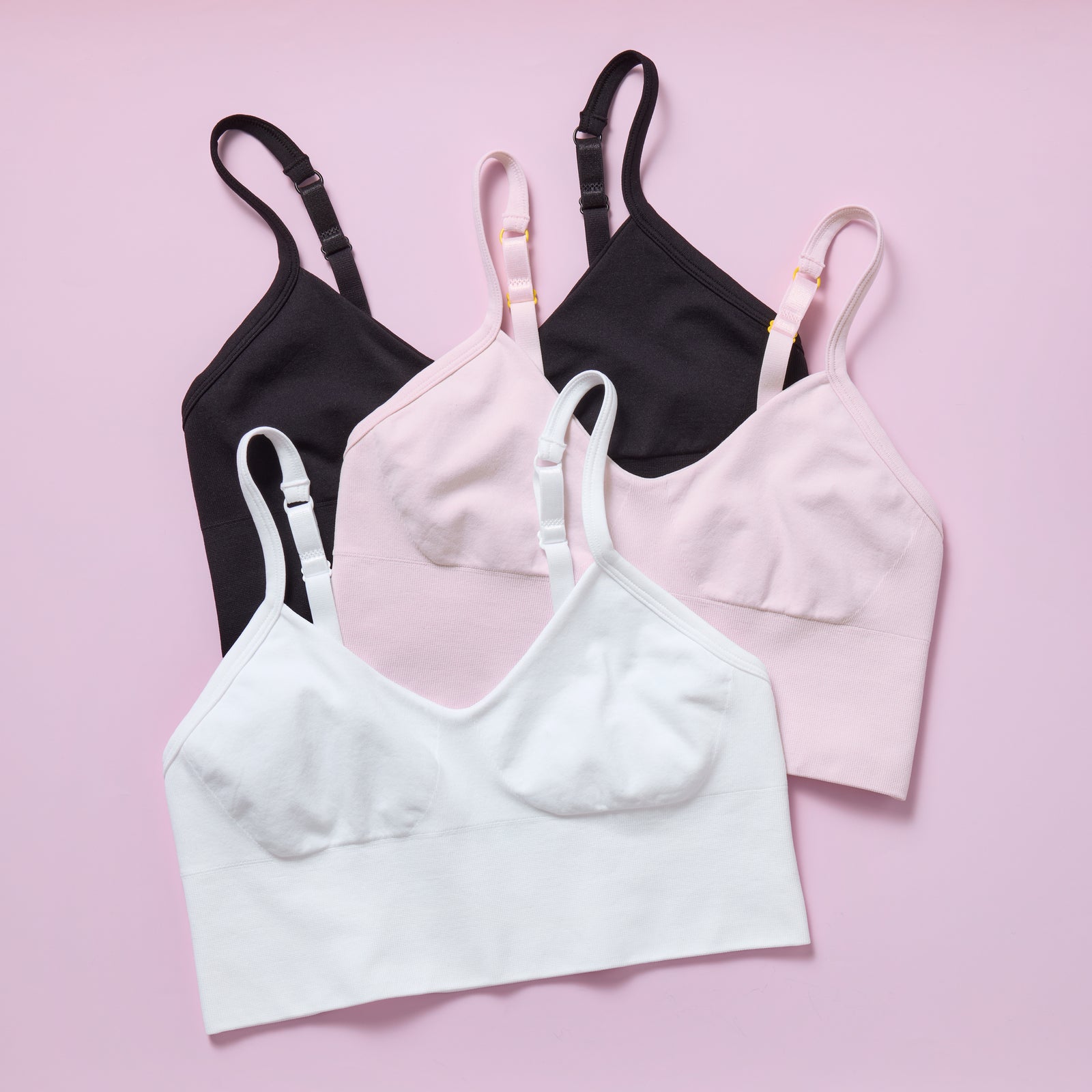 Three bras in black, white, and pink on a pink background