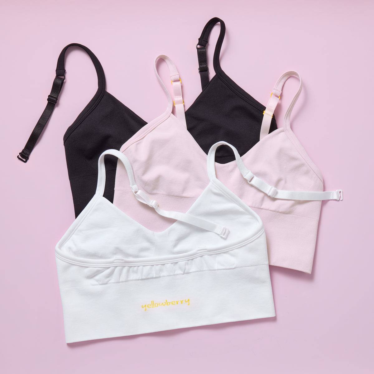 Set of women's bras in black, pink, and white on a pink background featuring the Yellowberry brand