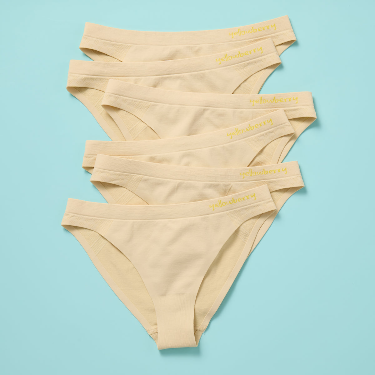 Six pairs of beige underwear stacked on a light blue background