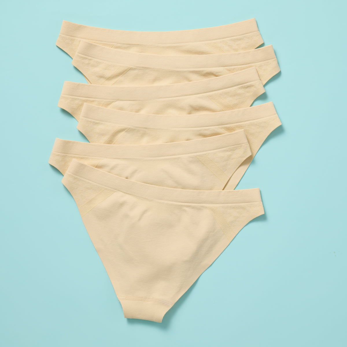 Six pairs of beige underwear stacked on a light blue background