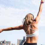 Yellowberry Awesome Tink Sports Bra in a soft brushed Nylon blend in a terrific new color, Storm. Easy pullover design with full support ensures a top drawer favorite. Storm is a great new neutral with a simple twist. The ultimate comfort for all-day wear. Girl in NYC building top against blue sky.
