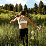 The Yellowberry Tulip Seamless Bra in Snowflake White photographed on model from the back with adjustable crisscross straps on Snow King against blue sky in the tall grass.