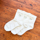 Three off-white crew socks with small embroidered tulip motifs in light blue and yellow, arranged on a rustic wooden surface.