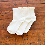 Three pairs of white ankle socks with ruffled edges, arranged on a rustic wooden surface.