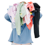 Girl holding a bunch of colorful cotton shirts in front of her face. The girl is wearing a long sleeve blue t-shirt
