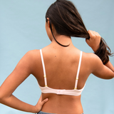 Woman wearing a light pink bralette against a light blue background