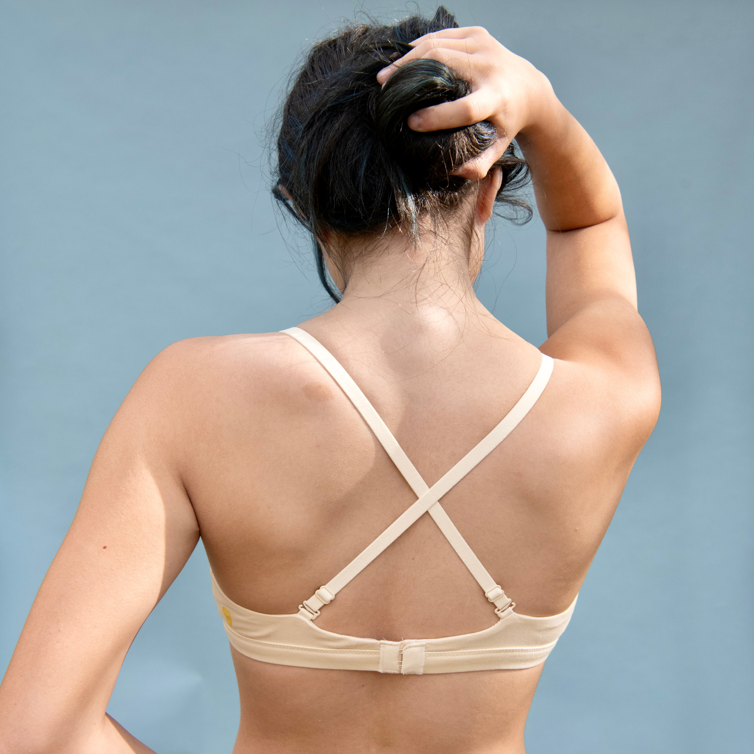 Woman wearing a beige bralette with criss-cross straps on a light blue background