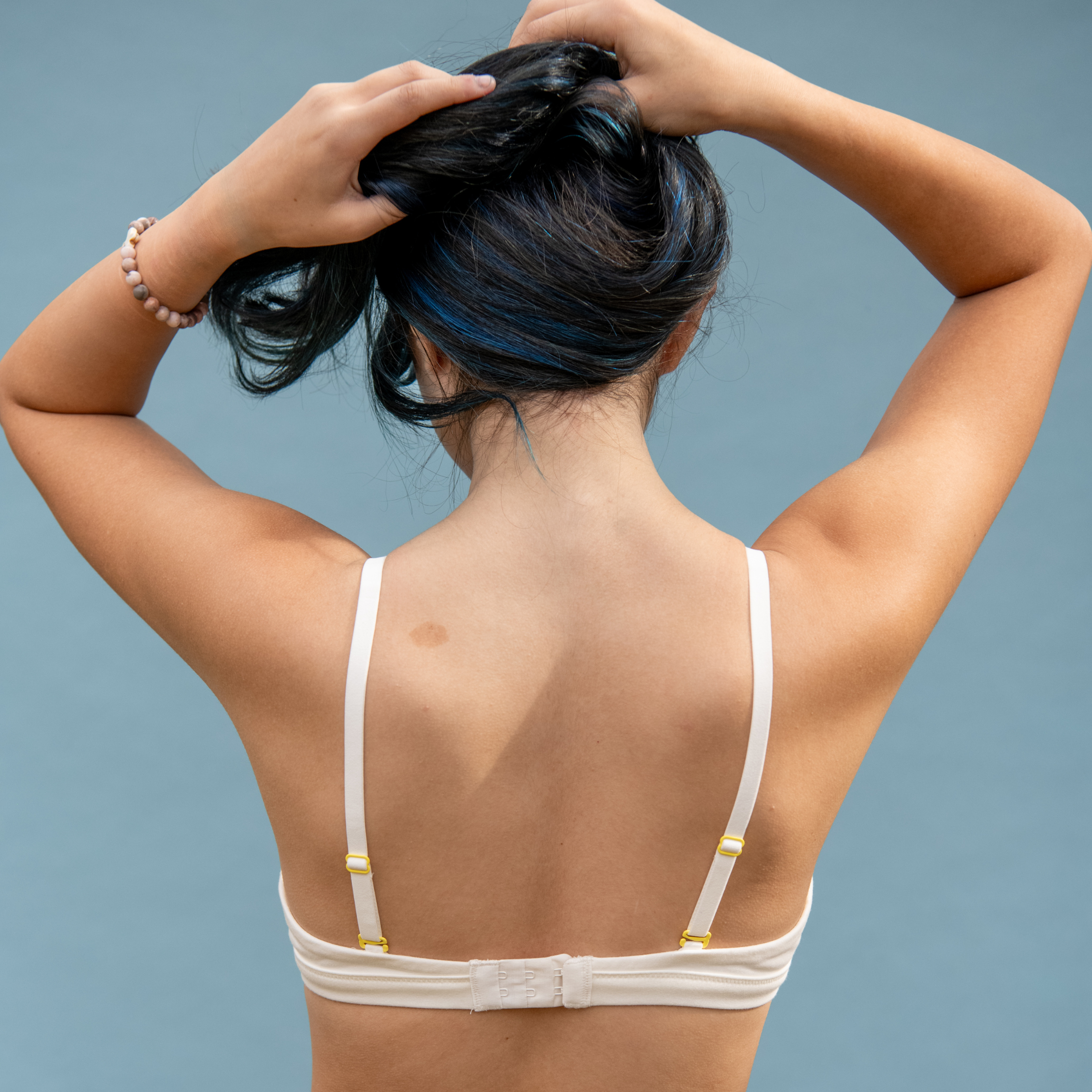 Person wearing a white bra with thin straps against a blue background