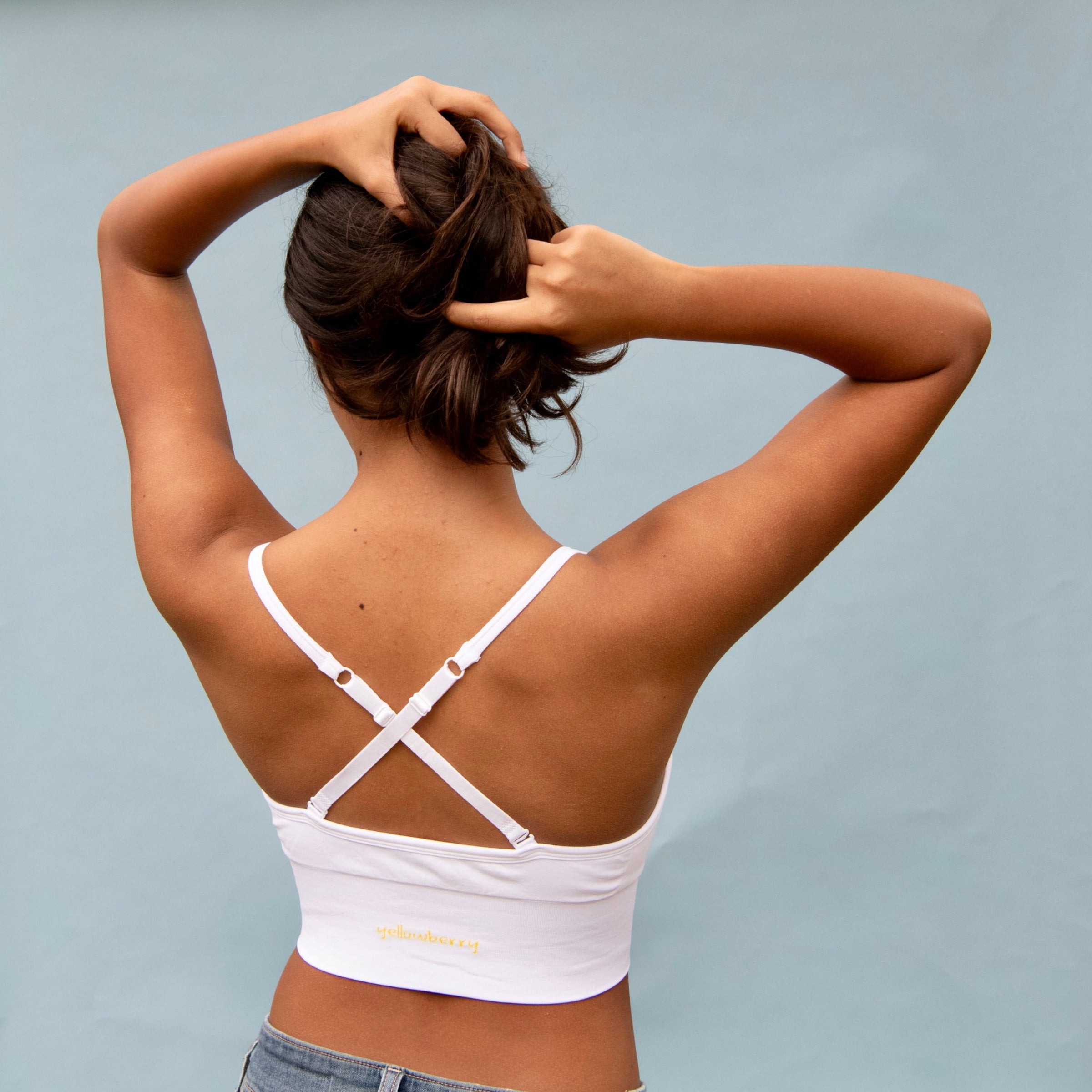 Person wearing a white sports bra with criss-cross straps on a blue background