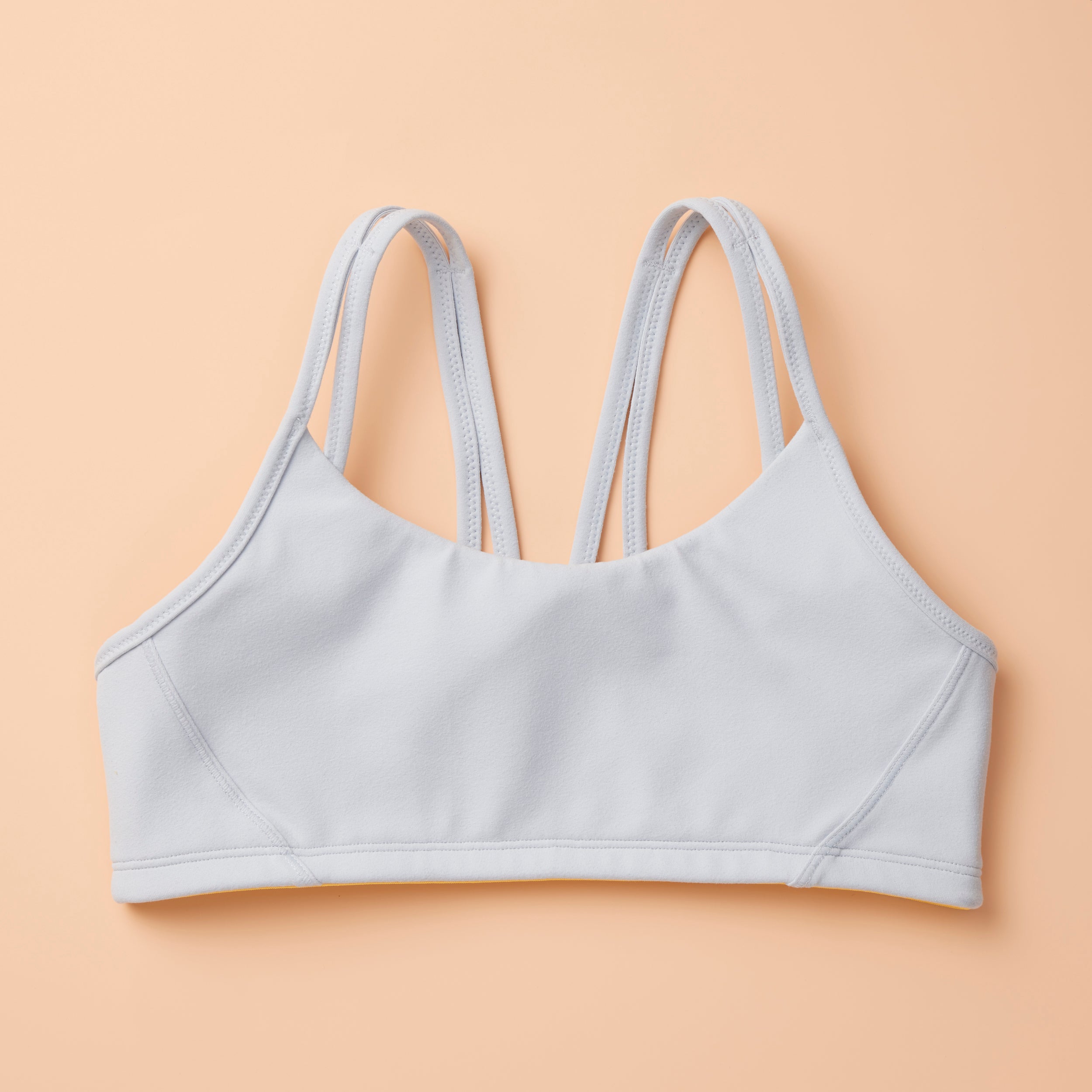 The Luna Bra by Yellowberry in Storm color, front laydown image. The Luna is one of Yellowberry's original hybrid styles; built specifically for girls to move seamlessly from the classroom to practice. It's like two bras in one! Features like smooth fabric and full coverage make the Luna a popular choice for girls looking for bras they can wear all day, every day.