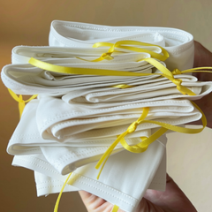 Stack of white face masks tied with yellow string against a neutral background