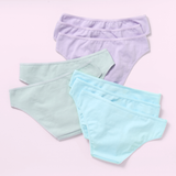 Eight pairs of women's bikini-style underwear in pastel colors, arranged in a flat-lay on a light pink background. The front pair is light aqua blue, the middle pair is mint green, and the back pair is light lavender purple.