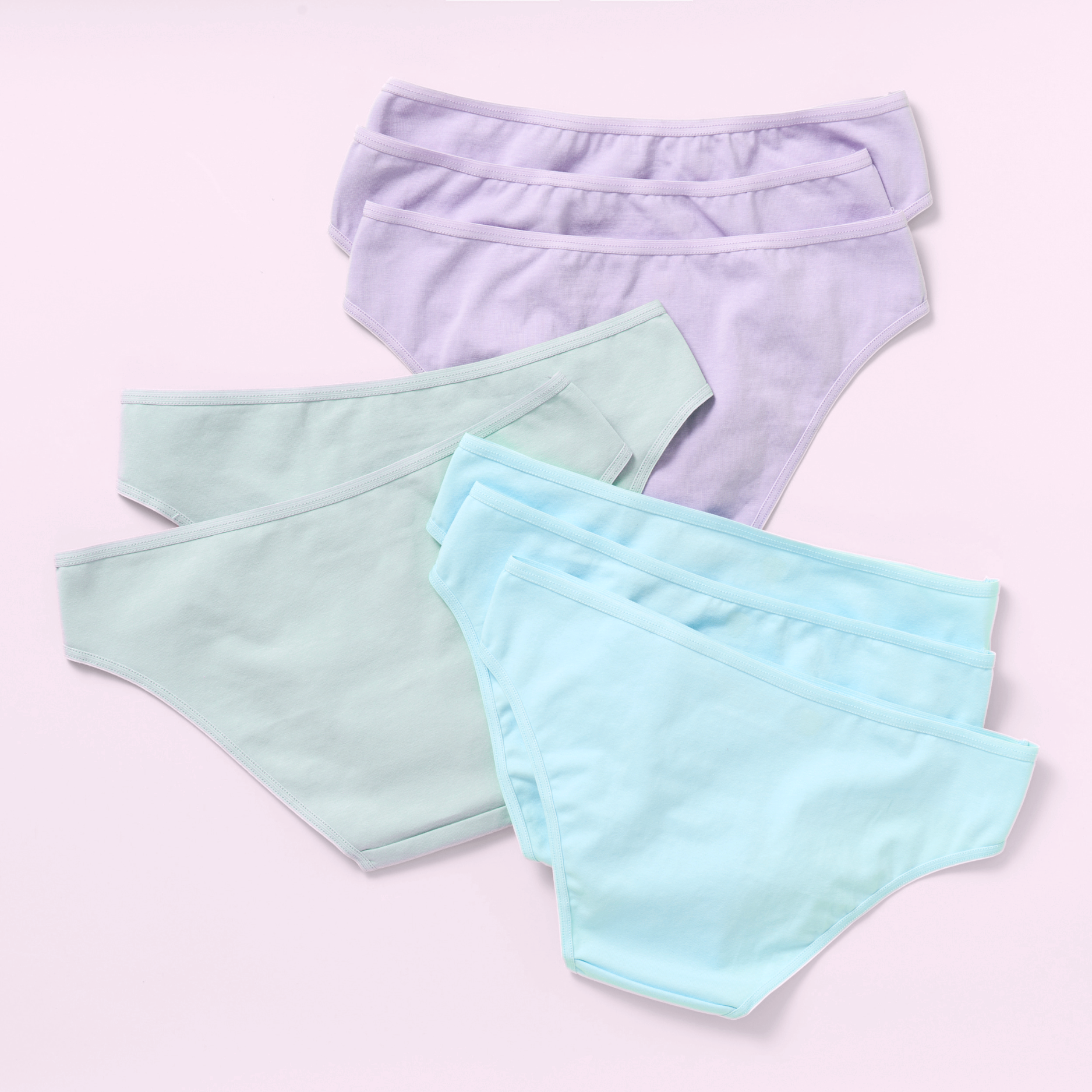 Eight pairs of women's bikini-style underwear in pastel colors, arranged in a flat-lay on a light pink background. The front pair is light aqua blue, the middle pair is mint green, and the back pair is light lavender purple.