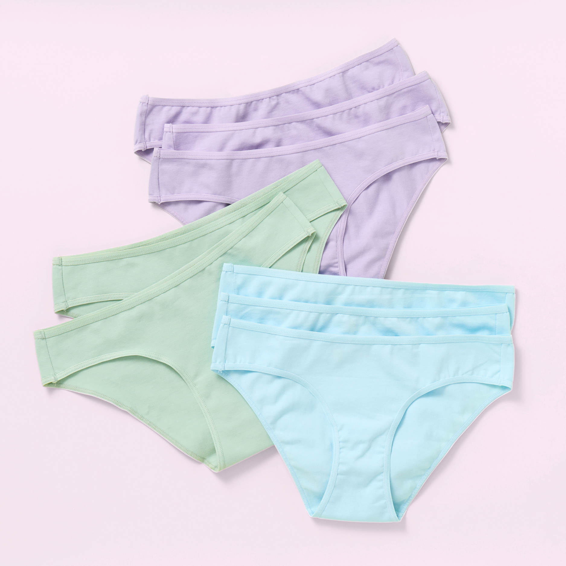 Eight pairs of women's high-waisted briefs in pastel colors, including light purple, mint green, and light blue, arranged in a fan shape on a solid light pink background.