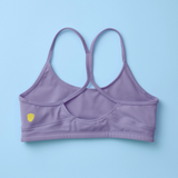 The back of a lavender purple sports bra with a crossover back strap design, laid flat on a light blue background.