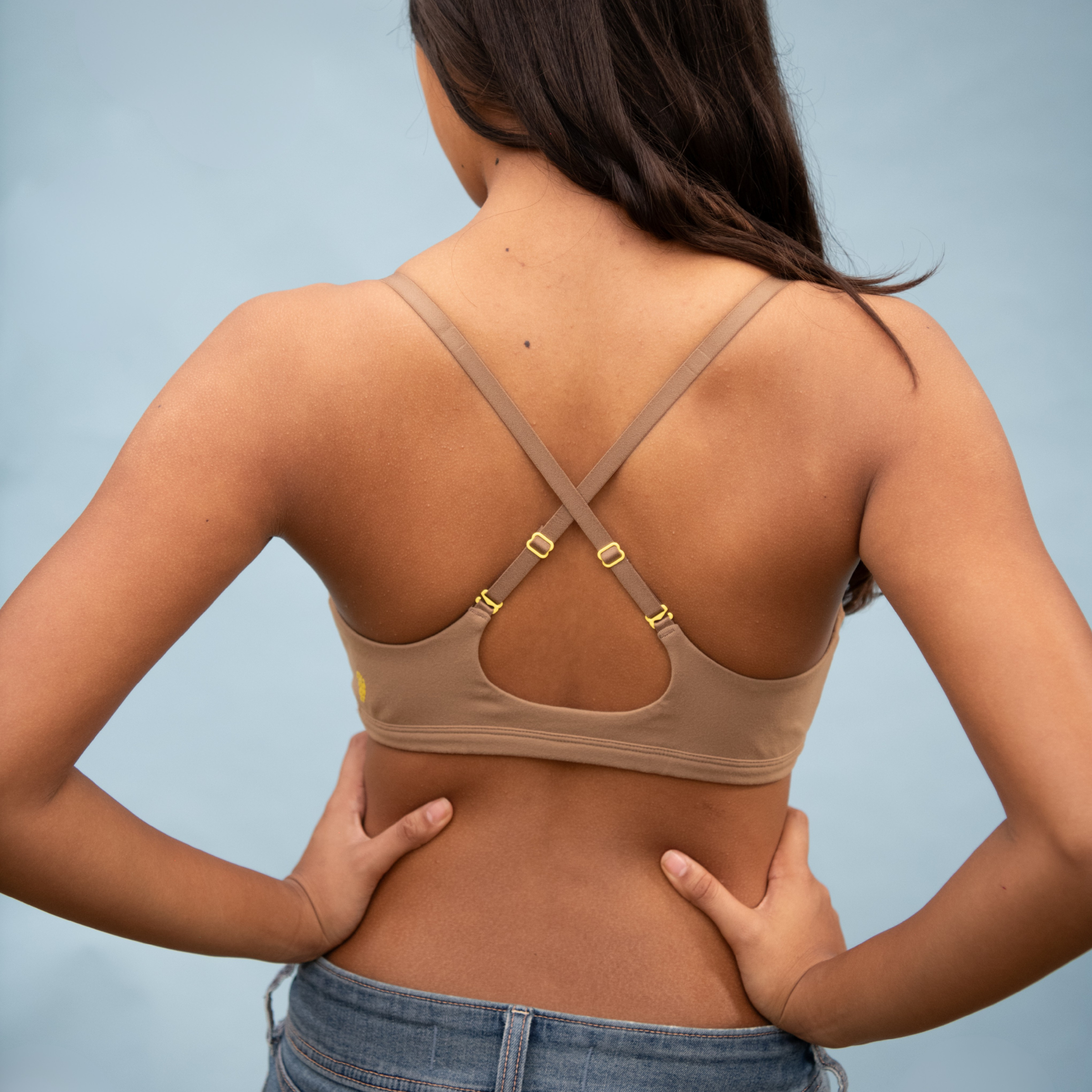 Woman wearing a nude sports bra with yellow buckles on a light blue background