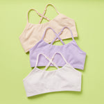 Three Ladybug Pima Cotton bras in the Summer colorway. All neutral colors, this 3PK Bundle of a white, beige and lavender selection of training bras on a green background.