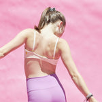 The Yellowberry Lily bra has plenty of room for growth, stretch, and change. Its chic design gives a little more definition and classic support than some of our other bras, and the back hook and eye clasp offers easy adjustments for the best fit. Lilly Bra back Doe Beige shown on model with purple leggings against pink seamless.