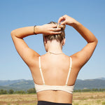 Yellowberry classic Lily bra has plenty of room for growth, stretch, and change. Its clean, simple design gives a little more definition and classic support than some of our other bras, with adjustable straps for the best fit. Lilly Bra on model in color Doe Beige against a meadow in Wyoming and mountains.