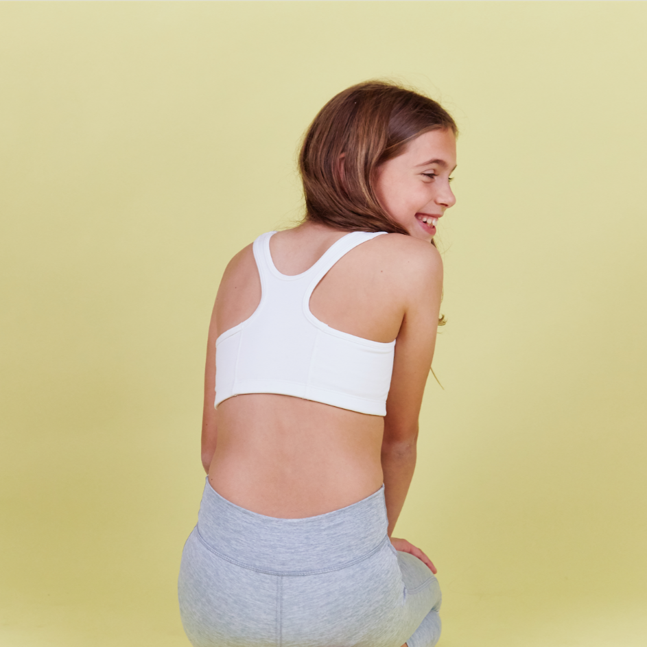 Girl wearing Half Moon Bra in white. The Yellowberry’s original sports bra. Newly redesigned and improved high-impact style. All natural fabrics. sweat-wicking, antimicrobial. Featuring a wider width racerback and buttery soft fabric. Great for sensitive skin.