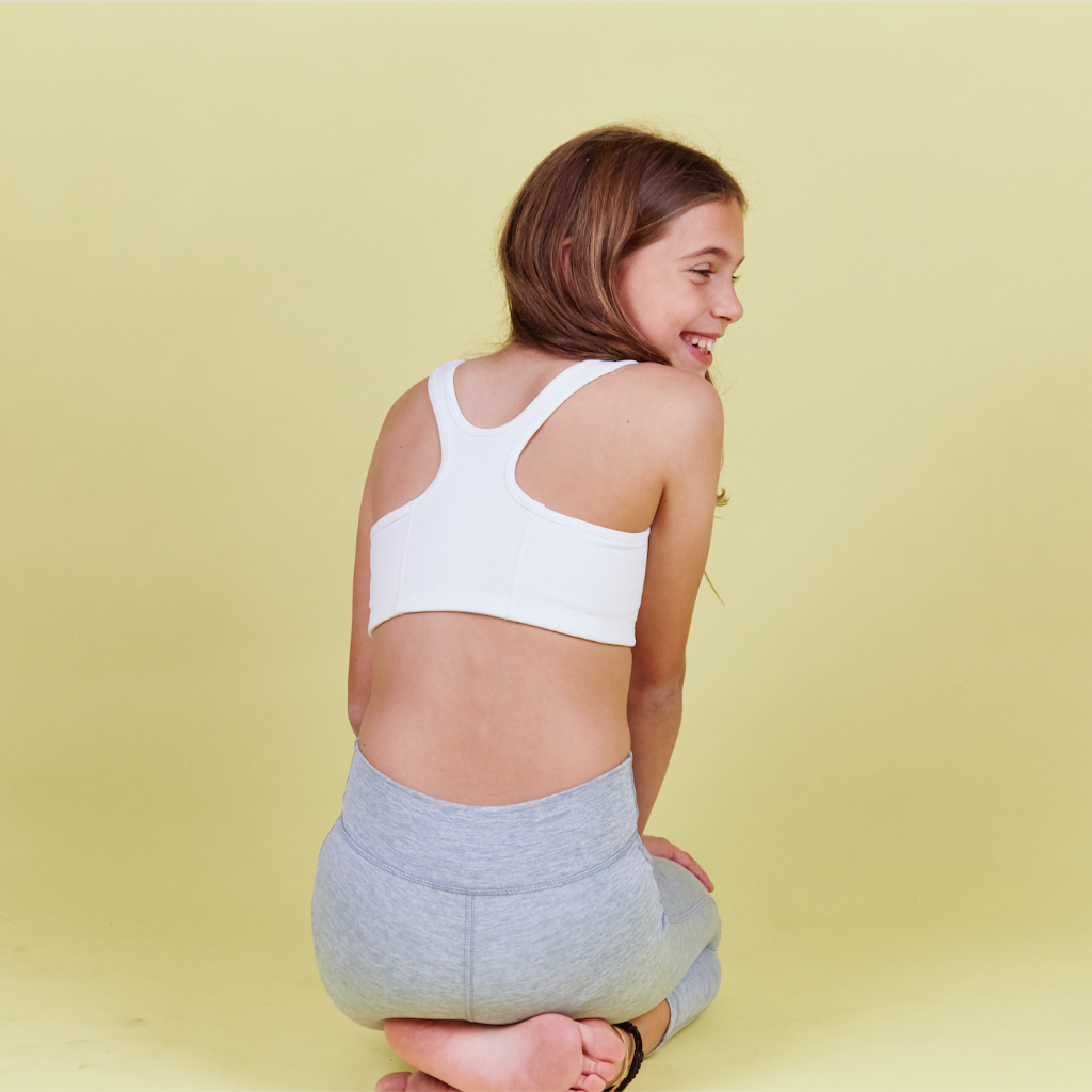 Girl wearing Half Moon Bra in white. The Yellowberry’s original sports bra. Newly redesigned and improved high-impact style. All natural fabrics. sweat-wicking, antimicrobial. Featuring a wider width racerback and buttery soft fabric. Great for sensitive skin.