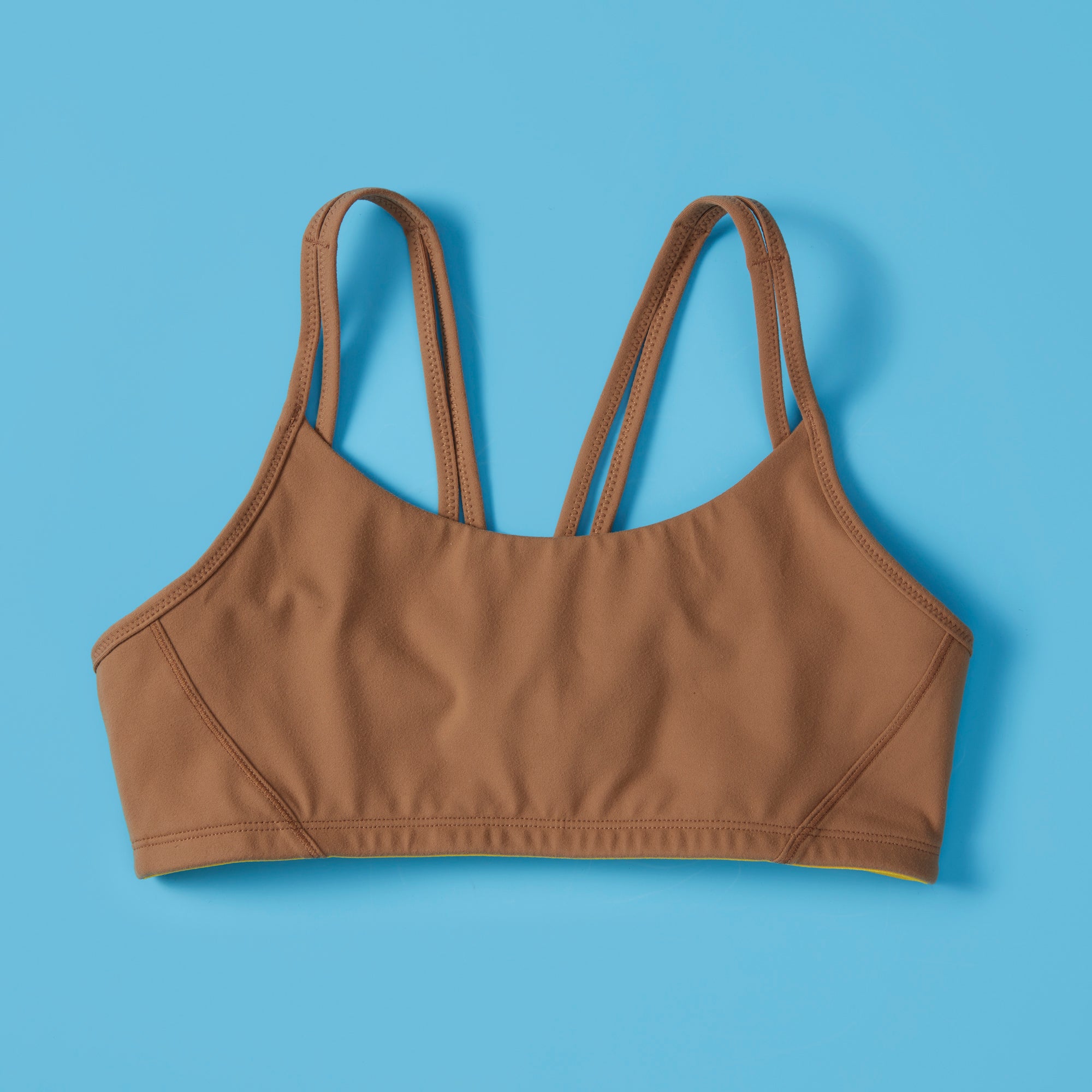 The Luna Bra by Yellowberry in Mocha color on blue background, front. The Luna is one of Yellowberry's original hybrid styles; built specifically for girls to move seamlessly from the classroom to practice. It's like two bras in one! Features like smooth fabric and full coverage make the Luna a popular choice for girls looking for bras they can wear all day, every day.